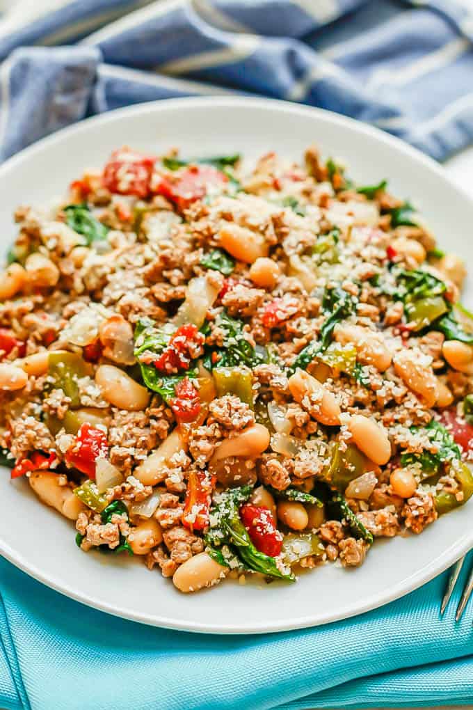 A ground turkey mixture with white beans, tomatoes and spinach served on a white plate with Parmesan cheese on top