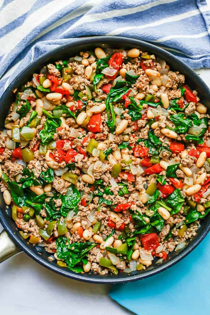 A skillet full of cooked ground turkey with onions, peppers, white beans, diced tomatoes and wilted spinach