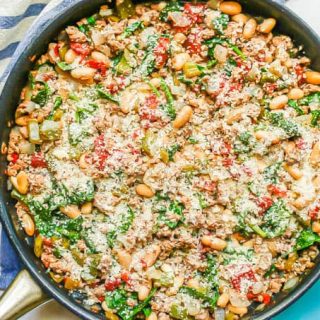 A large dark skillet with ground turkey, white beans, tomatoes and spinach with Parmesan cheese on top