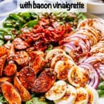 A spinach salad on a large white platter with roasted fingerling potatoes, sliced hard boiled eggs, red onion slices and sliced mushrooms, plus crumbled bacon and a bacon vinaigrette with a text overlay on the photo.