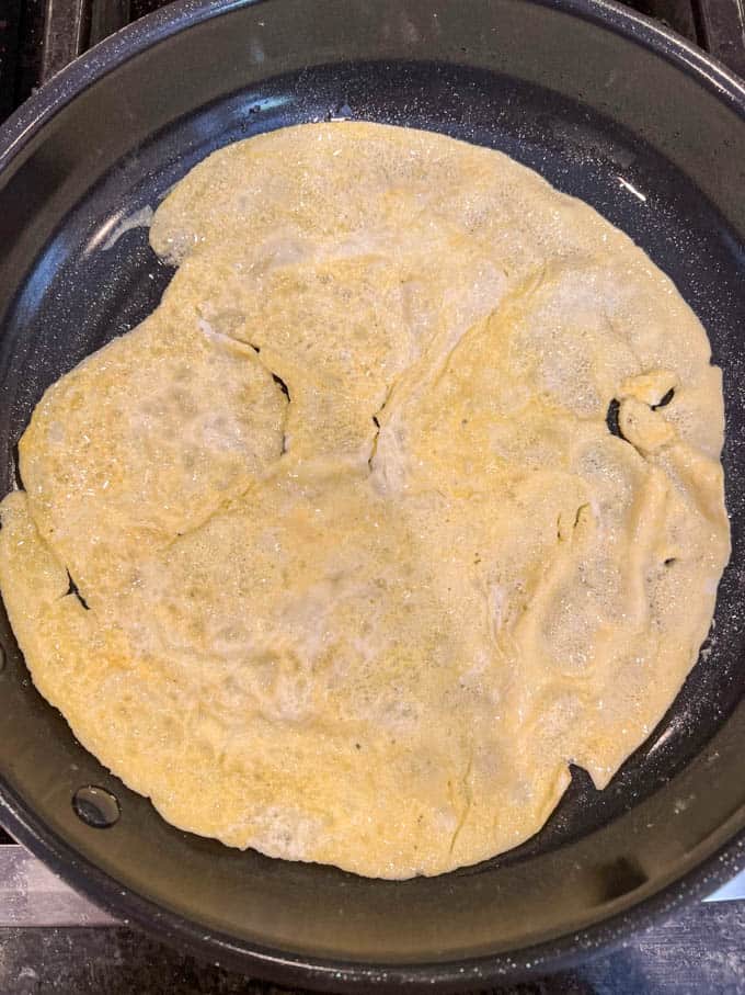 A flat omelet of cooked egg in a large skillet