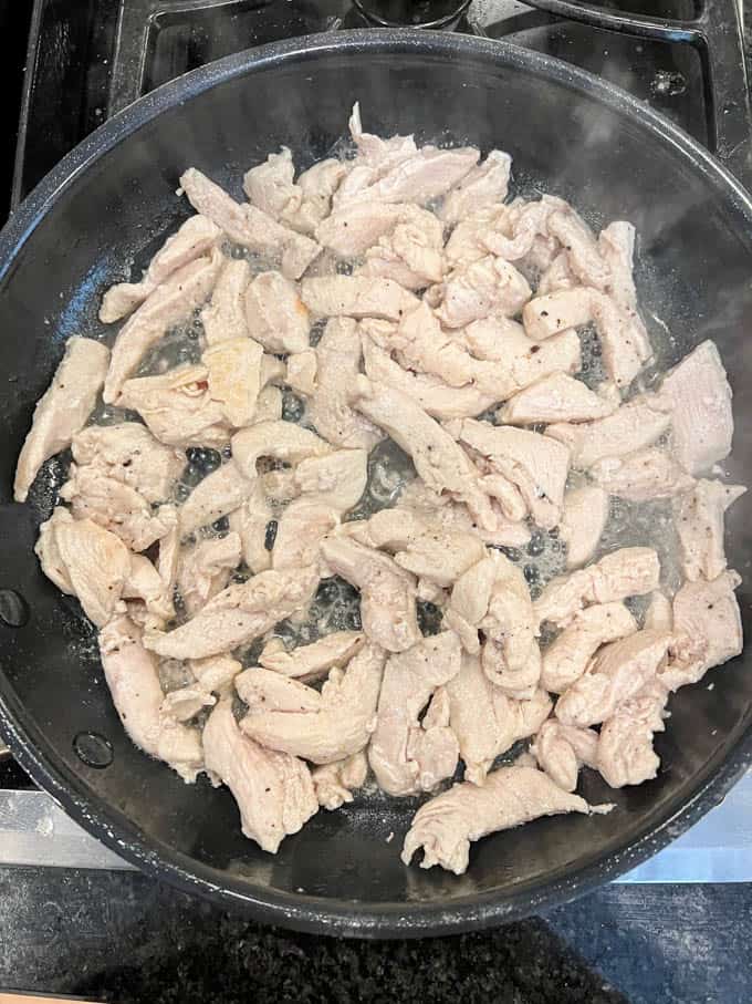 Strips of chicken cooking in a large skillet on the stove