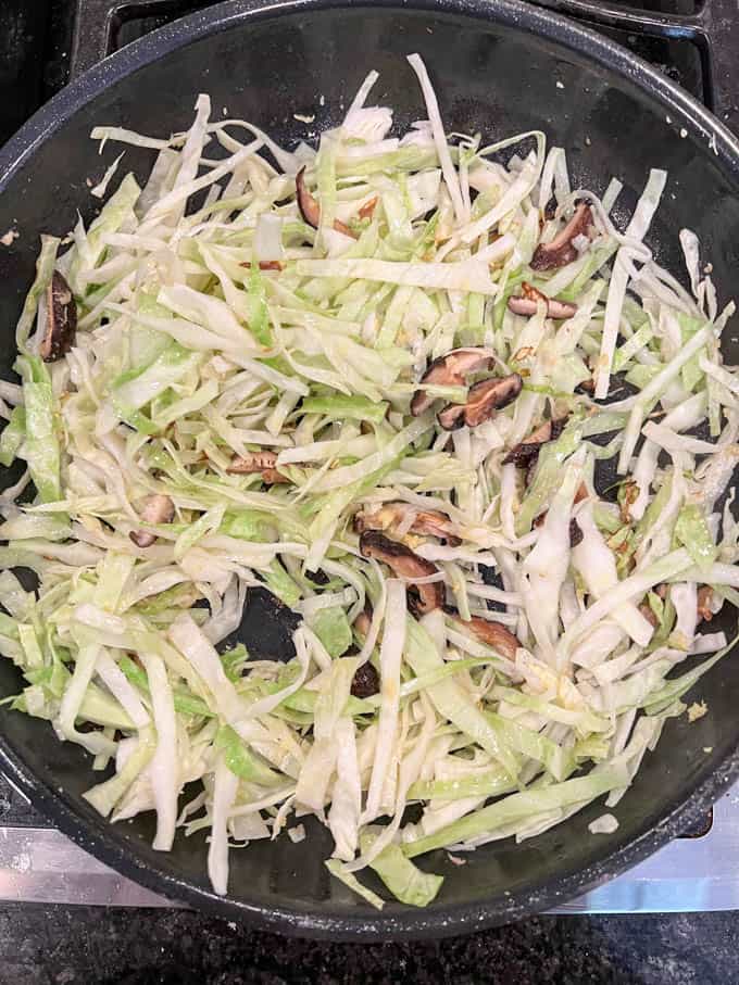 Wilted cabbage and mushrooms in a skillet on the stove