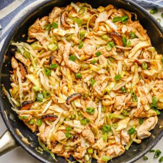 Moo shu chicken with cabbage, mushrooms and green onion in a large skillet with green onion slices to the side