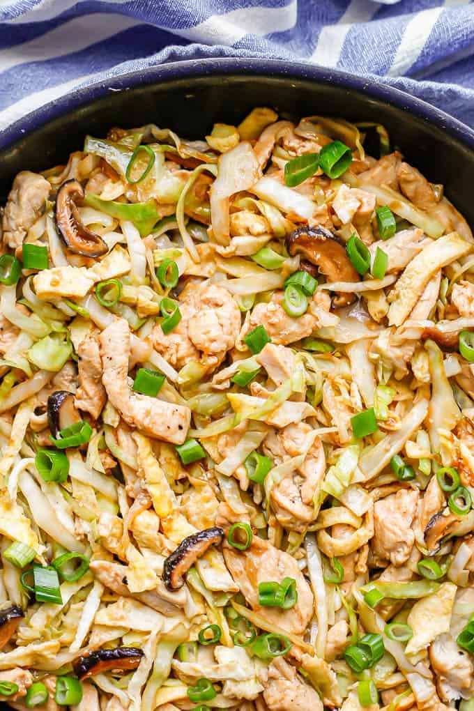 Close up of a large dark skillet with moo shu chicken with cabbage, mushrooms and egg topped with sliced green onions
