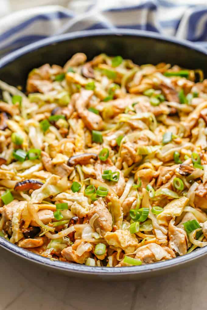 Side angle view of moo shu chicken cooked in a large dark skillet with green onions on top