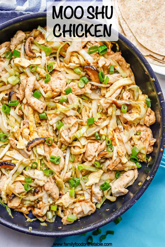A large skillet with moo shu chicken with cabbage, mushrooms, egg and green onion on top with a plate of tortillas to the side and a text overlay on the photo