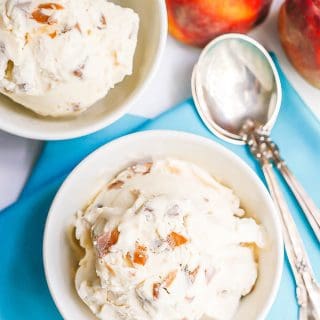 Two white bowls with scoops of homemade peach ice cream with some spoons and fresh peaches to the side