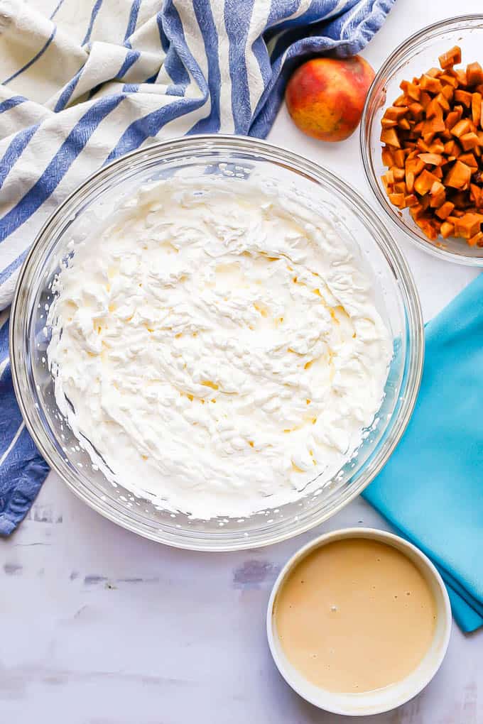 Ingredients for homemade peach ice cream in separate bowls on a white marble countertop