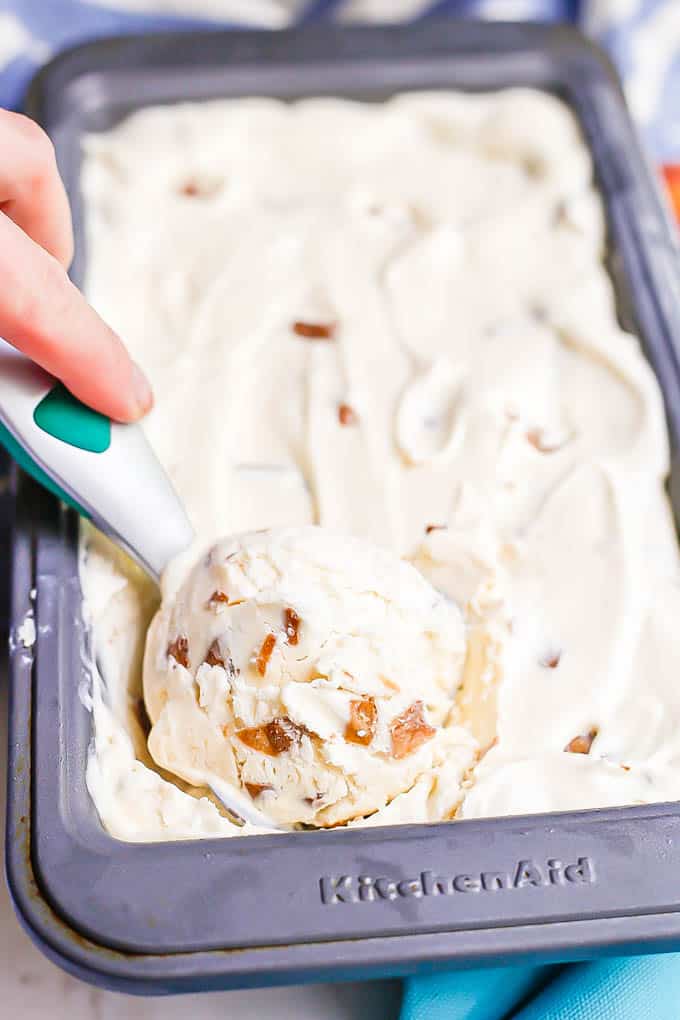 A hand scooping up some homemade peach ice cream from a container