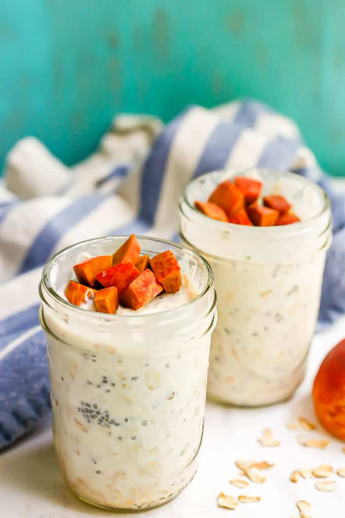 Two small glass jars of peach overnight oats with extra peaches on top