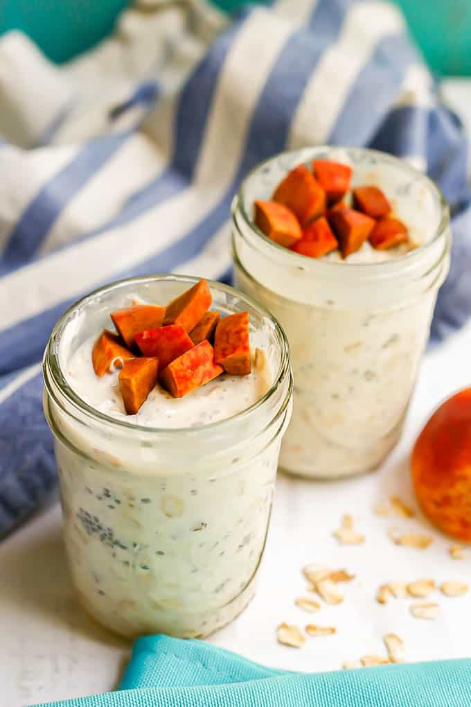 Two jars of peach overnight oats with extra peaches on top and a sprinkling of oats on the counter to the side