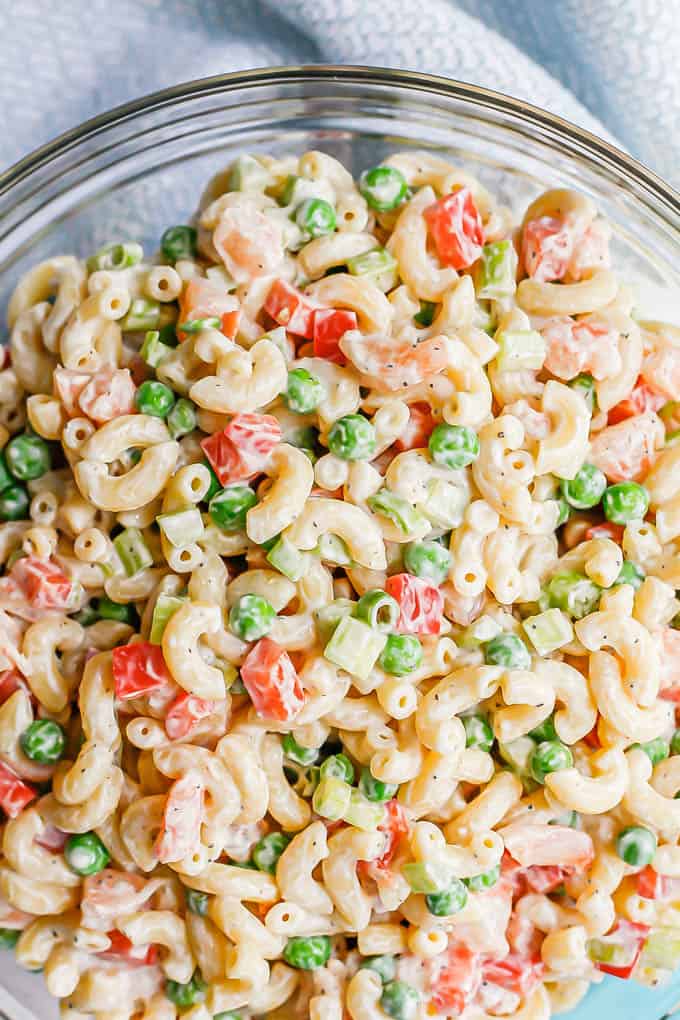 Close up of a cold, creamy shrimp pasta salad with peas and bell pepper in a large glass bowl