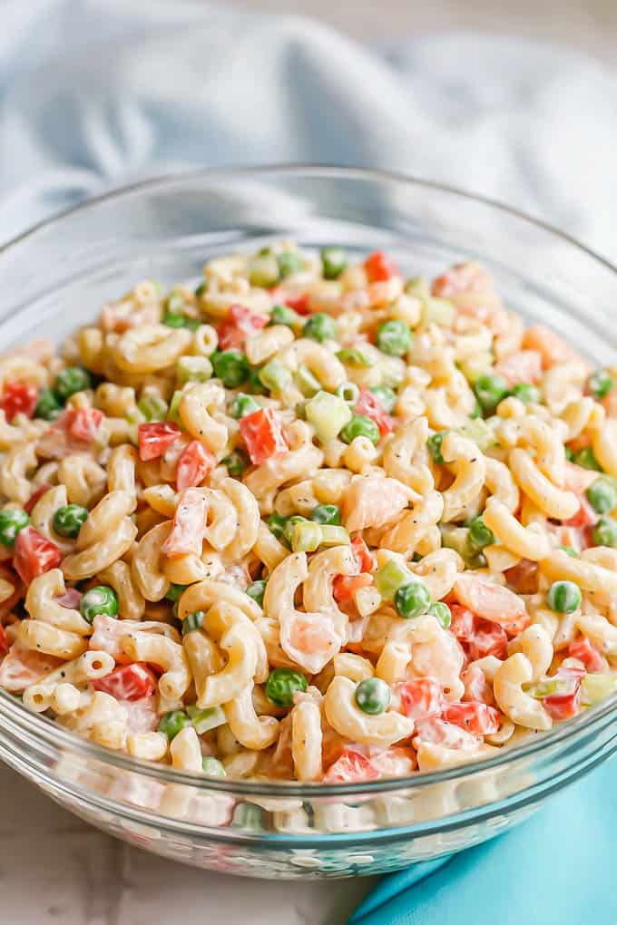 A cold, creamy pasta salad with peas, bell peppers and small shrimp pieces served in a large glass bowl