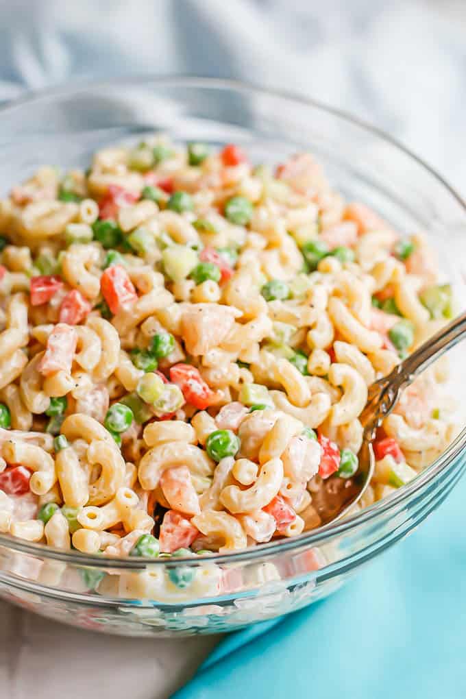 A spoon scooping up some pasta salad with shrimp and peas and bell peppers from a large glass bowl