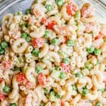 A cold, creamy shrimp pasta salad with peas and bell pepper in a large glass bowl with a text overlay on the image