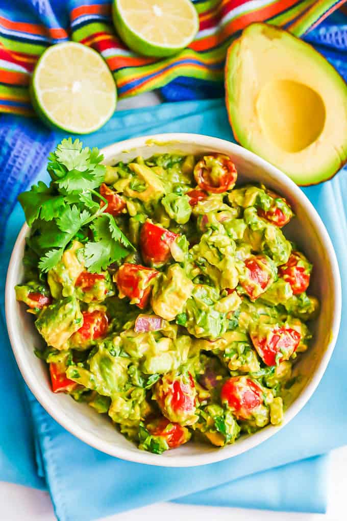 A creamy tomato avocado salad with cilantro sprigs and a cut lime and avocado to the side