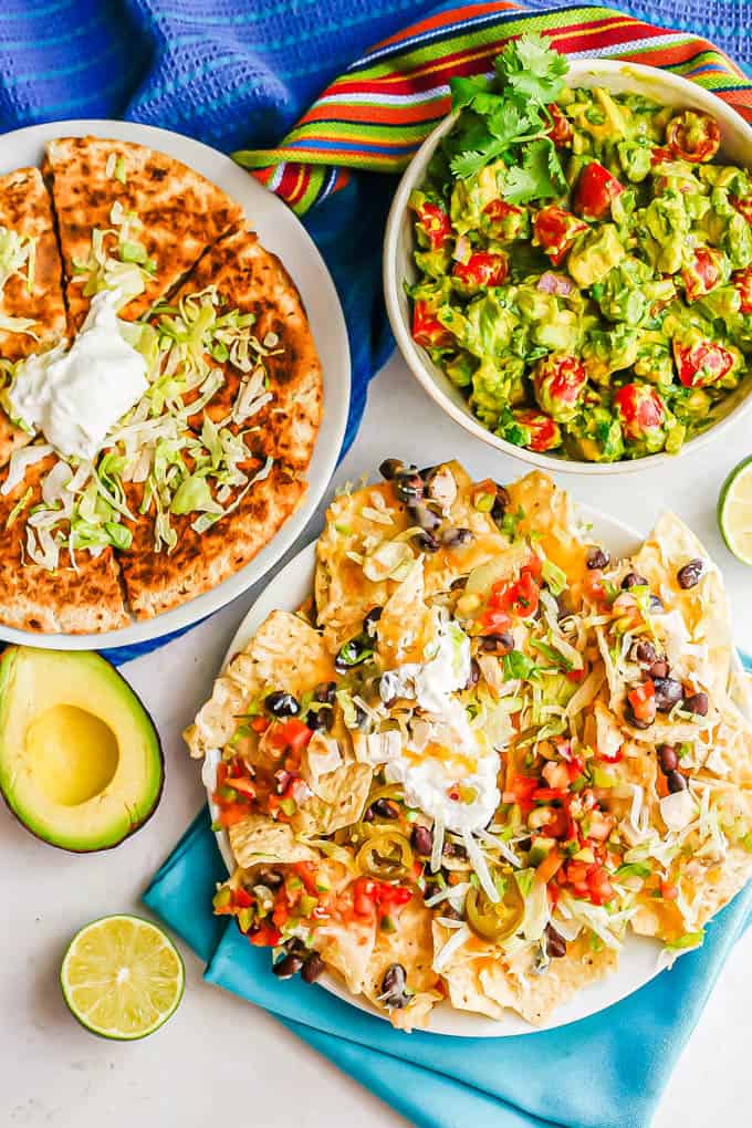 Fiesta spread with quesadillas, loaded chicken nachos and avocado salad with colorful napkins scattered