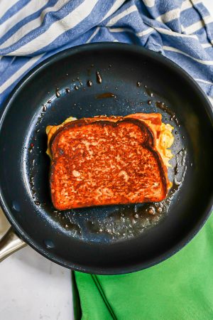 A golden brown breakfast grilled cheese being cooked in a dark skillet