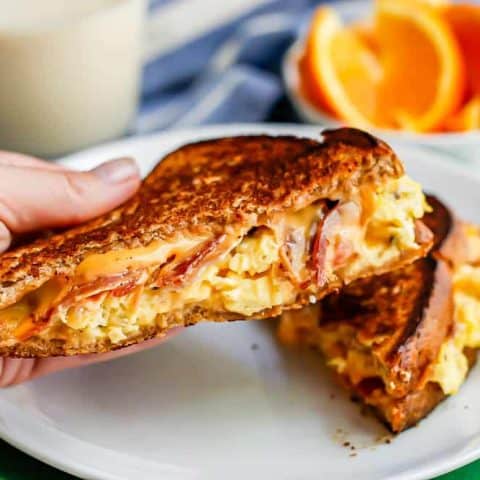 A hand picking up a breakfast grilled cheese sandwich from a white plate