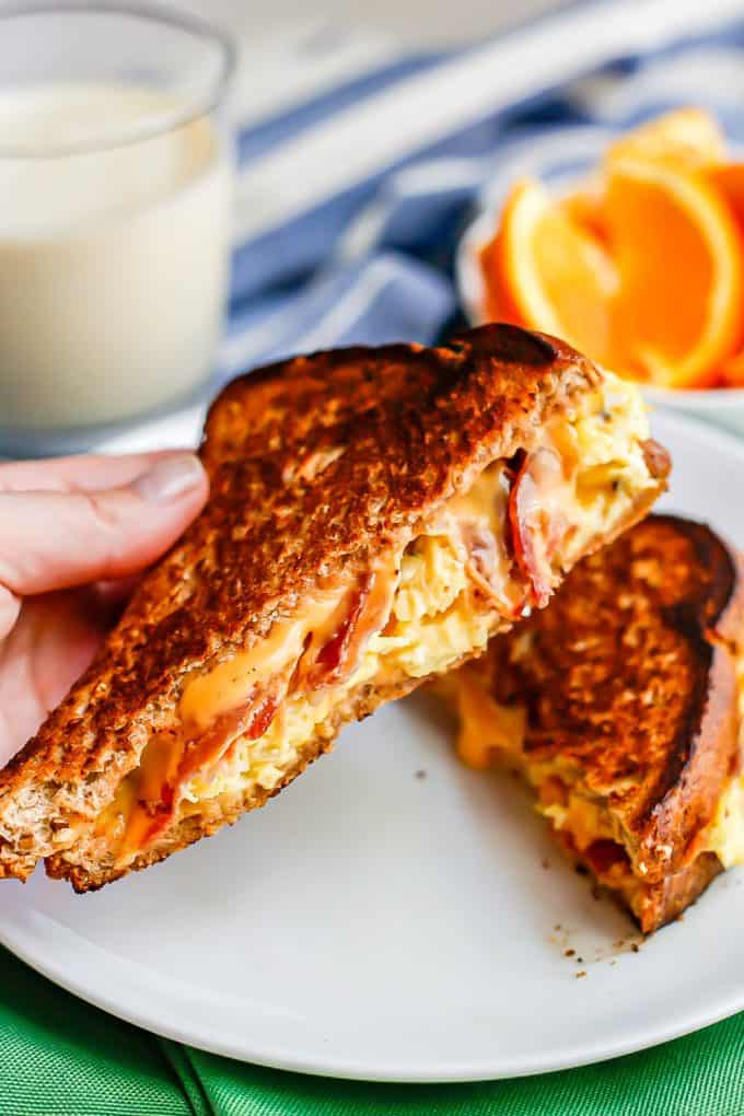 Close up of a hand holding a bacon, egg and cheese grilled cheese sandwich