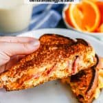 A hand holding up a half of a grilled cheese with bacon and scrambled eggs from a white plate with a text overlay on the photo