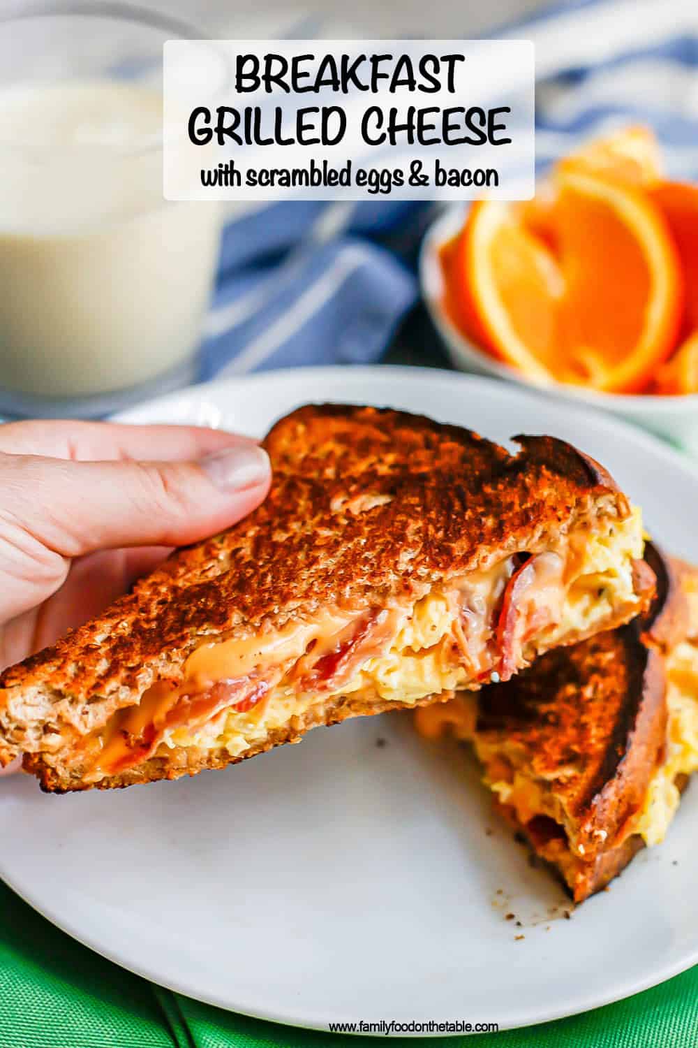 A hand holding up a half of a grilled cheese with bacon and scrambled eggs from a white plate with a text overlay on the photo