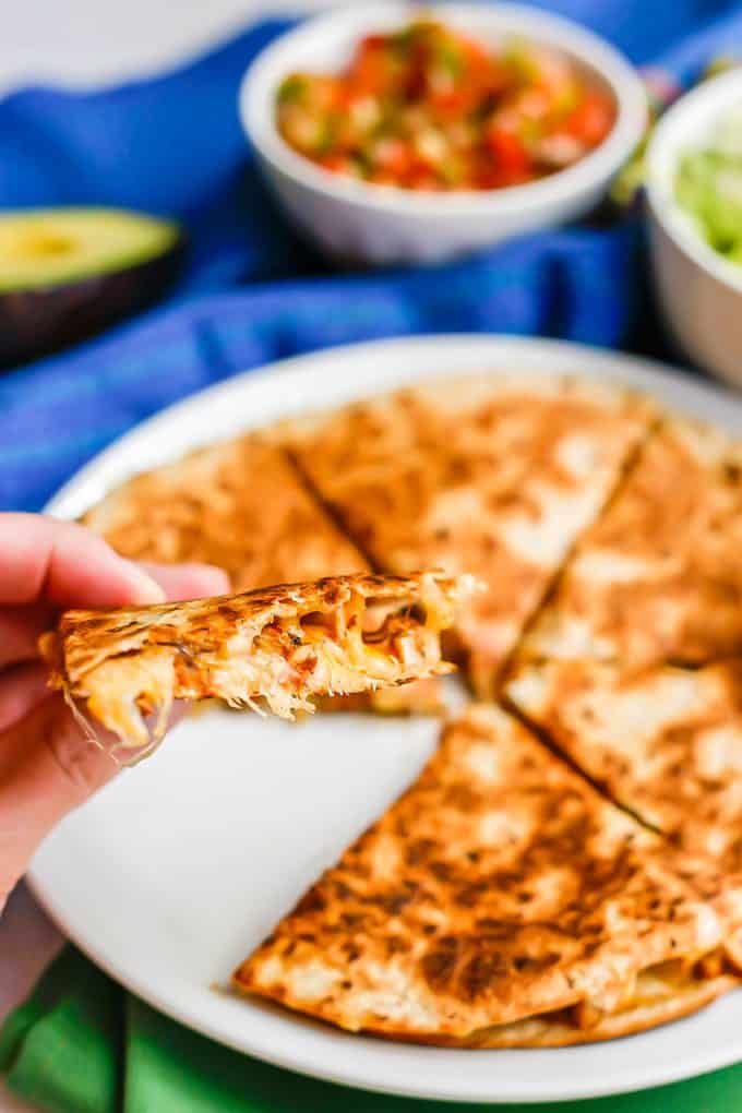 A cheesy chicken quesadilla being held up from a plate after being cooked