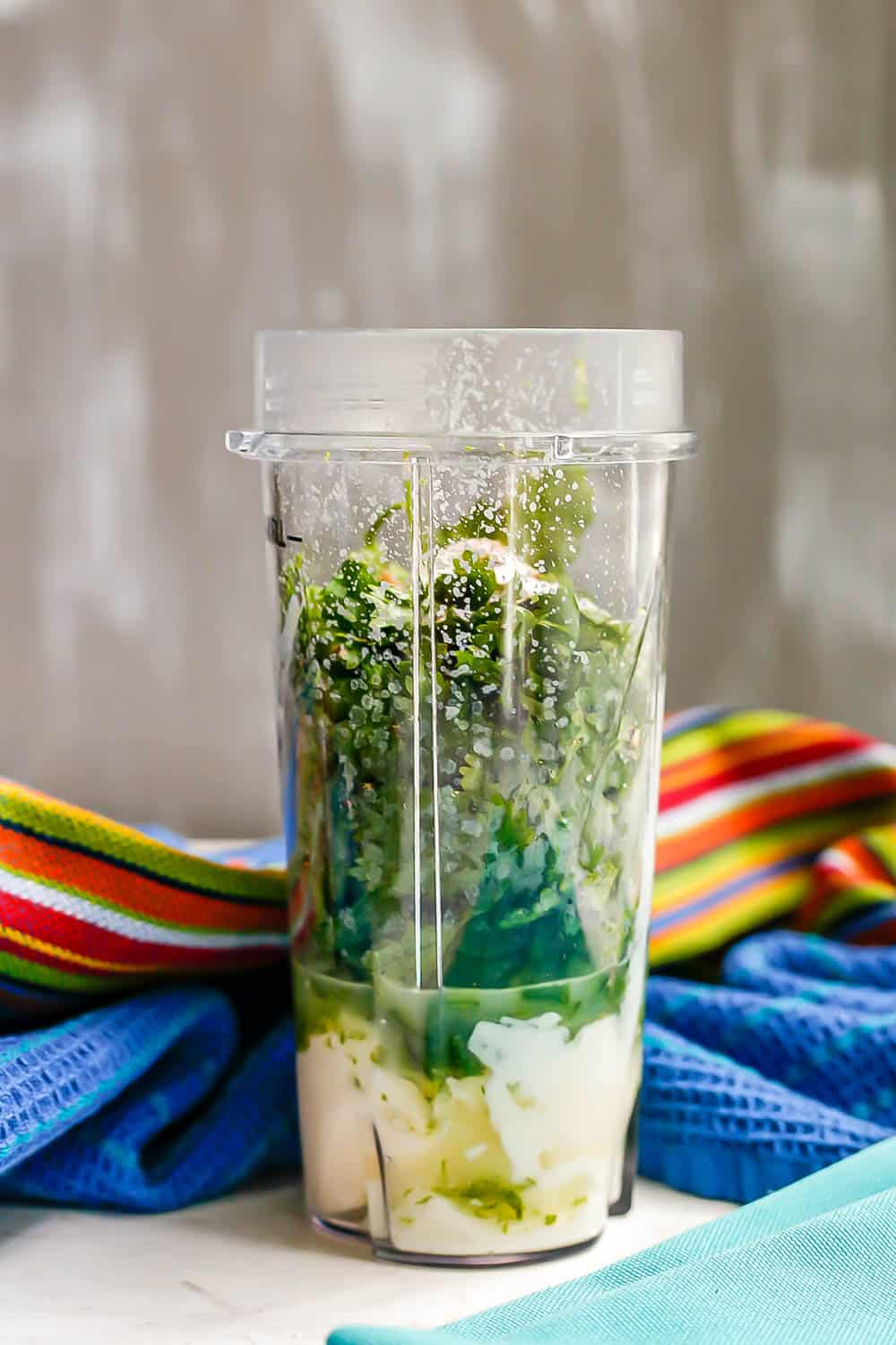 A small blender cup with Greek yogurt, mayo, lime juice, cilantro and other ingredients layered in for making cilantro lime dressing