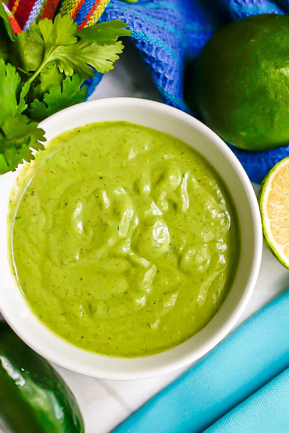 Close up of cilantro lime dressing in a small white bowl with colorful napkins to the side