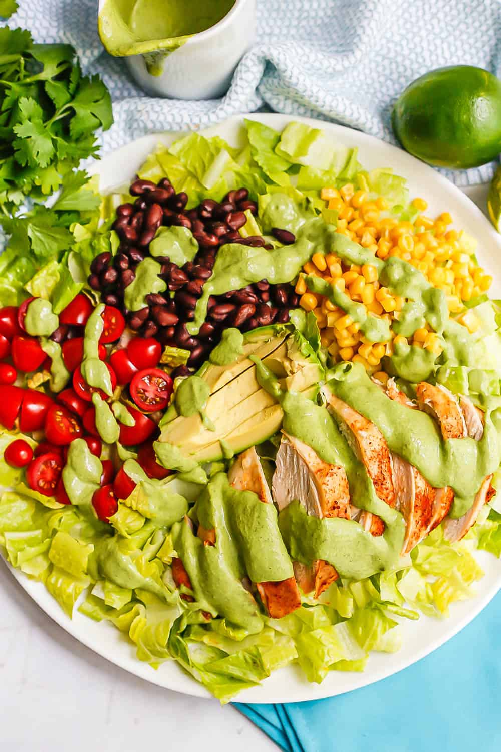 A southwestern style salad with romaine, tomatoes, black beans, corn and sliced chicken breast on a white platter with a cilantro lime dressing drizzled all over top