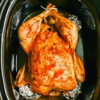 A seasoned and cooked whole chicken in a crock pot with the drumsticks tied