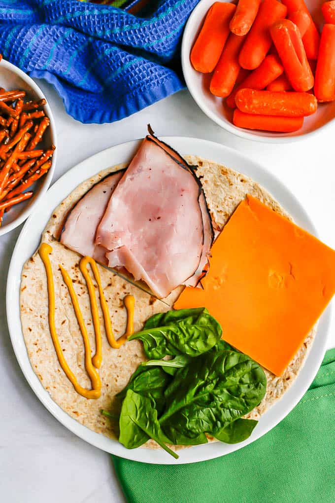 A tortilla with mustard, ham, sliced cheddar and spinach before being folded up