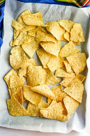 An even layer of tortilla chips on a parchment paper lined baking sheet