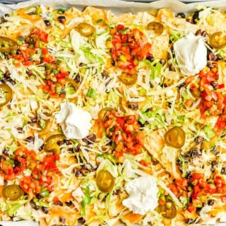 A sheet pan full of loaded chicken nachos with black beans and cheese with lettuce, jalapeños, salsa and Greek yogurt as toppings on top