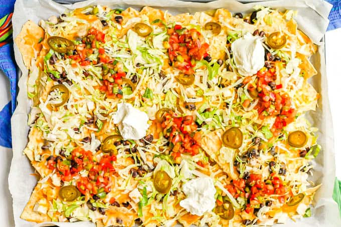 A sheet pan full of loaded chicken nachos with black beans and cheese with lettuce, jalapeños, salsa and Greek yogurt as toppings on top