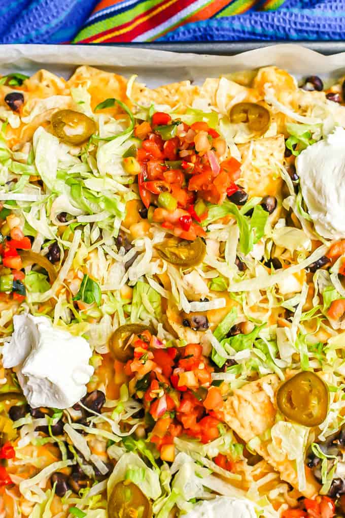 Chicken nachos on a baking sheet with pico de gallo, Greek yogurt, shredded lettuce and pickled jalapeños on top
