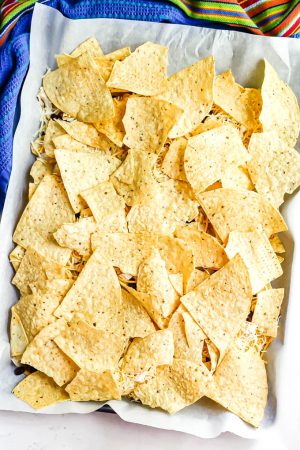 A second layer of tortilla chips being added to sheet pan nachos