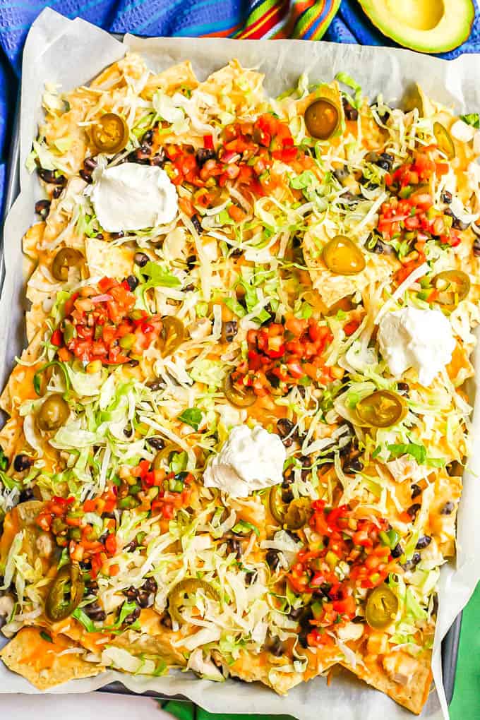 Sheet pan chicken nachos with black beans and cheese with lettuce, jalapeños, salsa and Greek yogurt as toppings on top