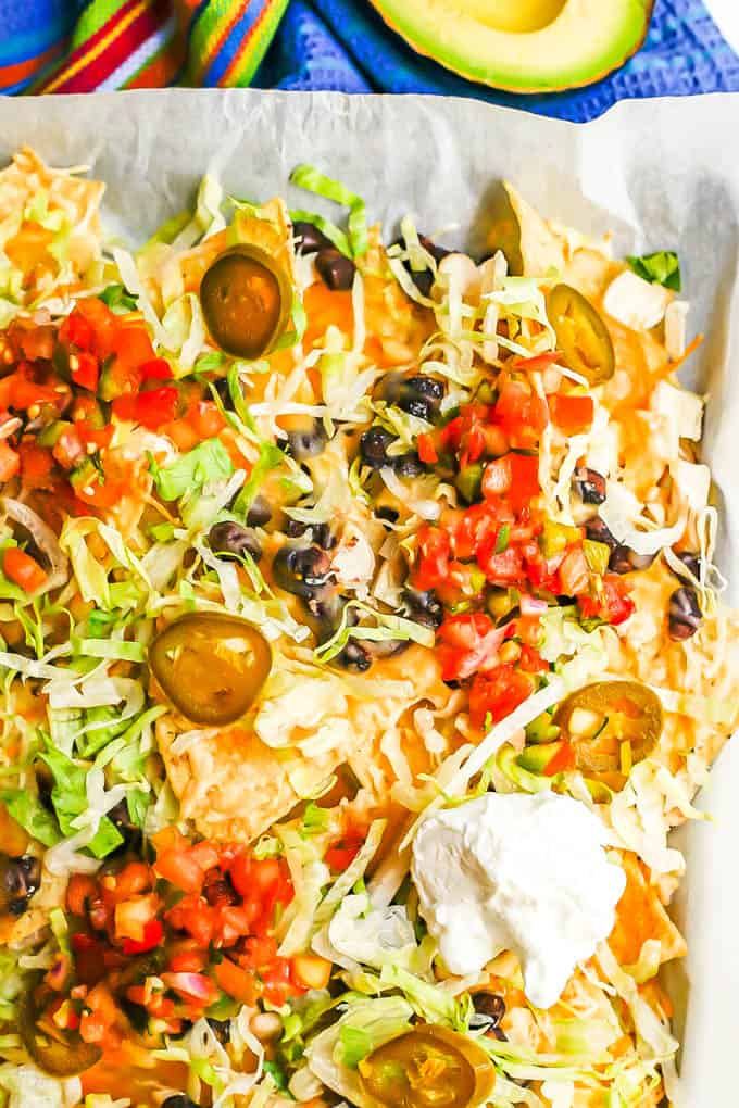 Close up of sheet pan chicken nachos with black beans and cheese with lettuce, jalapeños, salsa and Greek yogurt as toppings on top