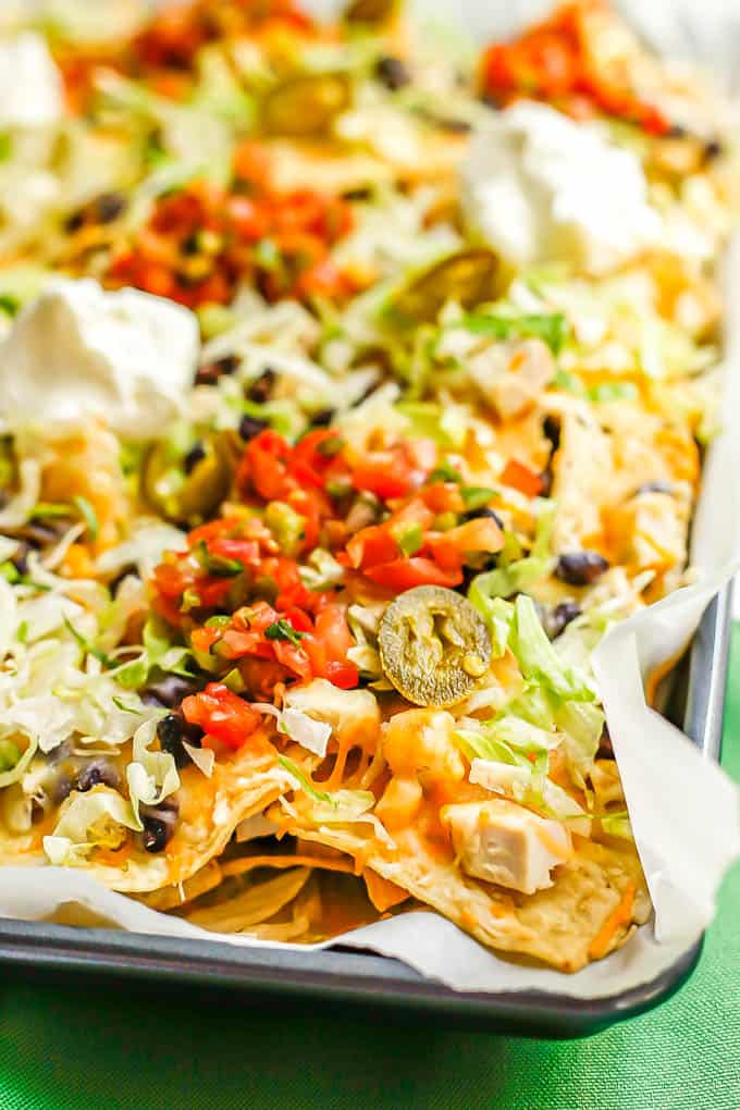 Side angle close up of sheet pan chicken nachos with black beans and cheese with lettuce, jalapeños, salsa and Greek yogurt as toppings on top