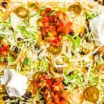 Chicken nachos on a baking sheet with pico de gallo, Greek yogurt, shredded lettuce and pickled jalapeños on top with a text overlay on the photo