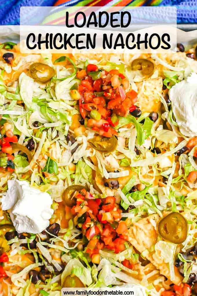 Chicken nachos on a baking sheet with pico de gallo, Greek yogurt, shredded lettuce and pickled jalapeños on top with a text overlay on the photo