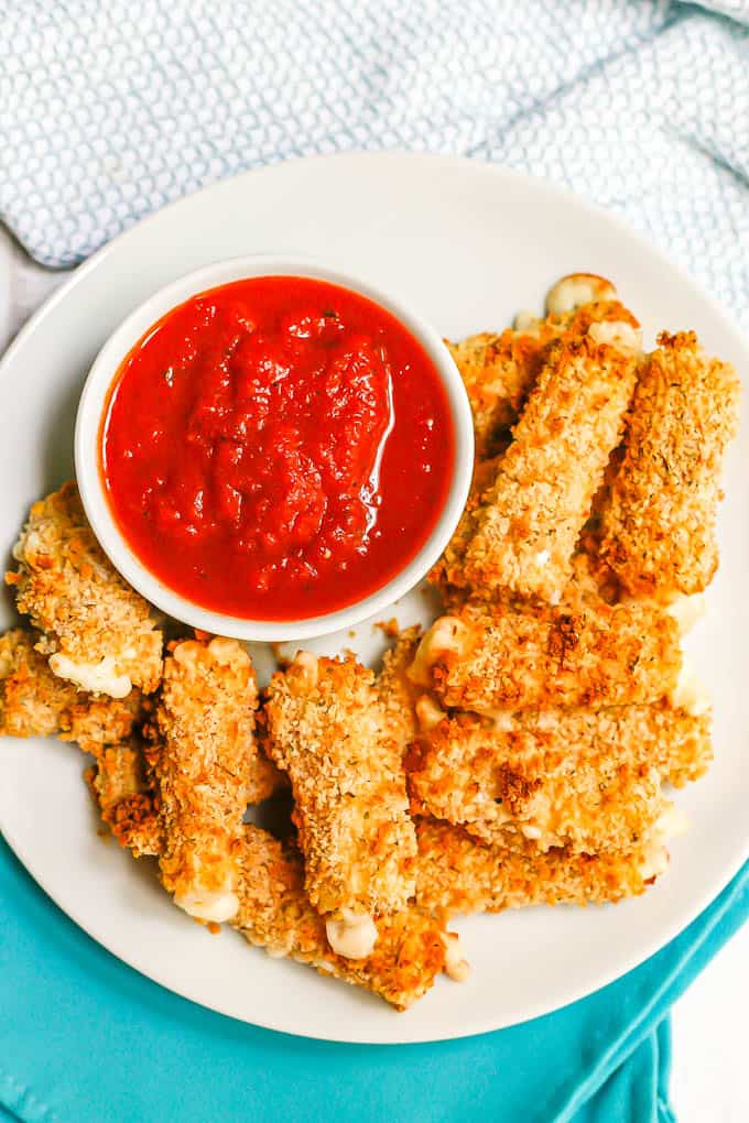 A round white plate with homemade mozzarella sticks and a small bowl of marinara sauce for dipping