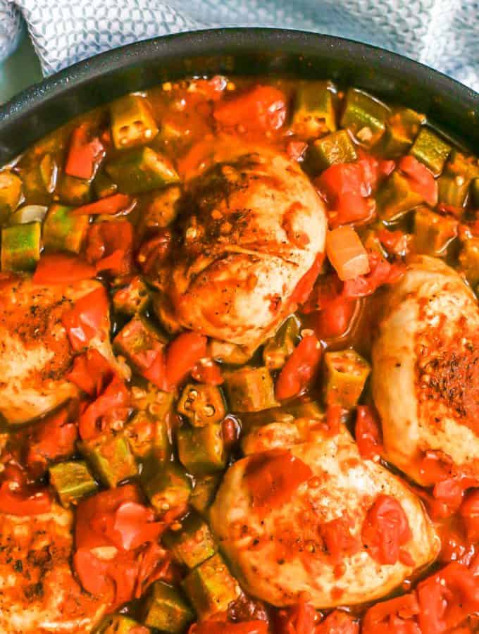 Close up of seared seasoned Cajun chicken and okra in a skillet with tomatoes and veggies