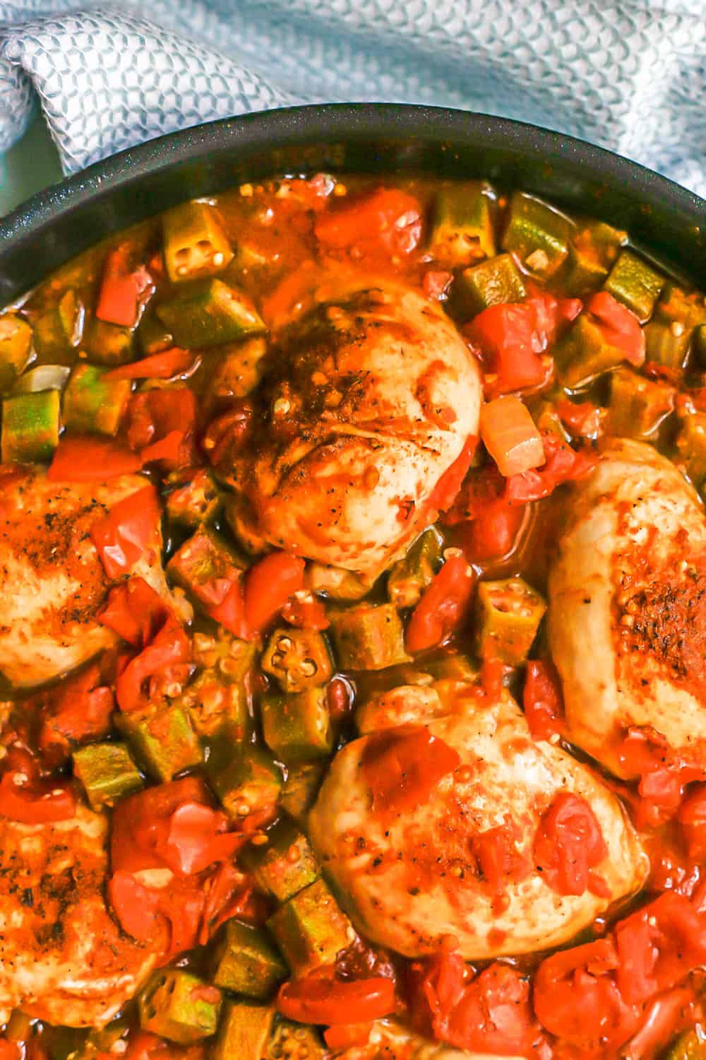 Close up of seared seasoned Cajun chicken and okra in a skillet with tomatoes and veggies