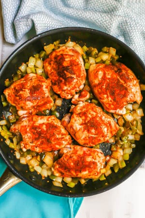 Seared chicken thighs in a skillet with onion, green pepper and celery