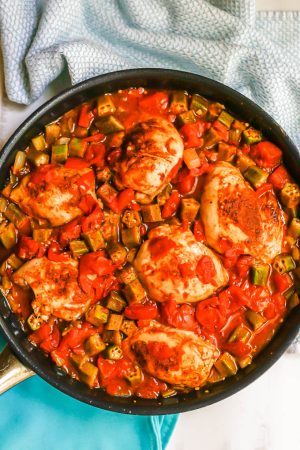 Cajun chicken thighs with okra, tomatoes and veggies in a large dark skillet