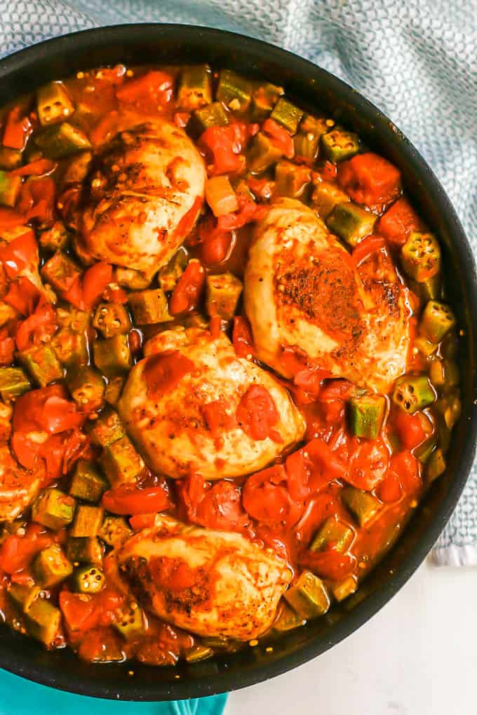 Close up of seared Cajun chicken thighs with tomatoes and okra in a large dark skillet