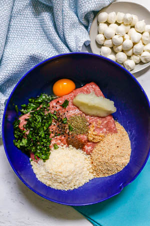 Ingredients for mozzarella stuffed Caprese meatballs being put together in a large blue bowl